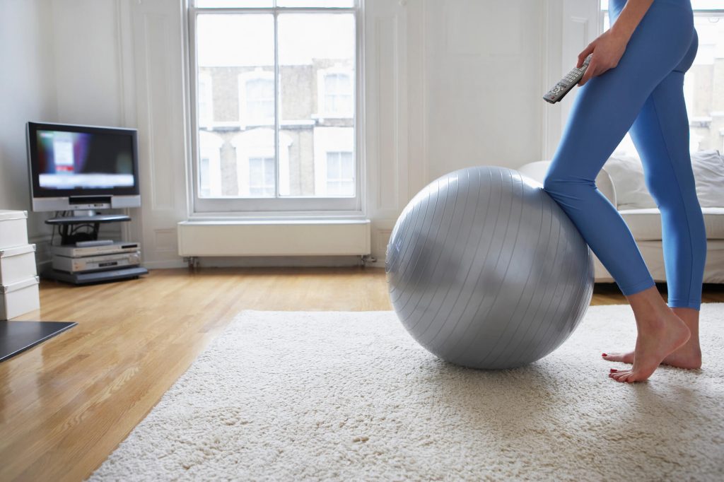 mulher se exercitando em bola de pilates em frente à tv